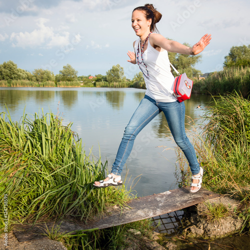 Portrait of young lady in a jeans with handbag jumping by the lake