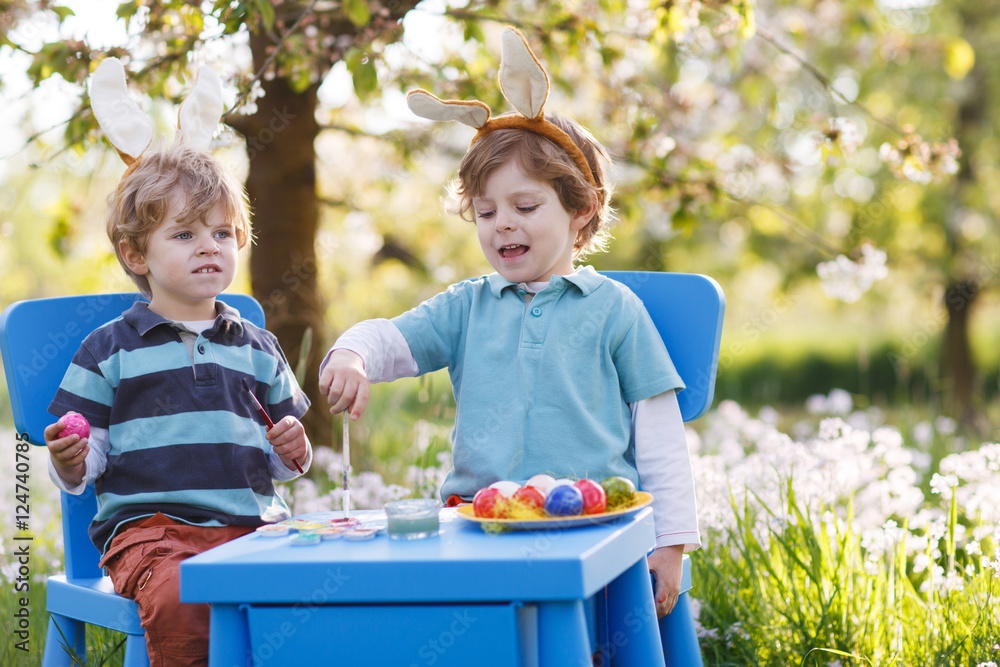 Two little boys wearing Easter bunny ears, painting colorful egg