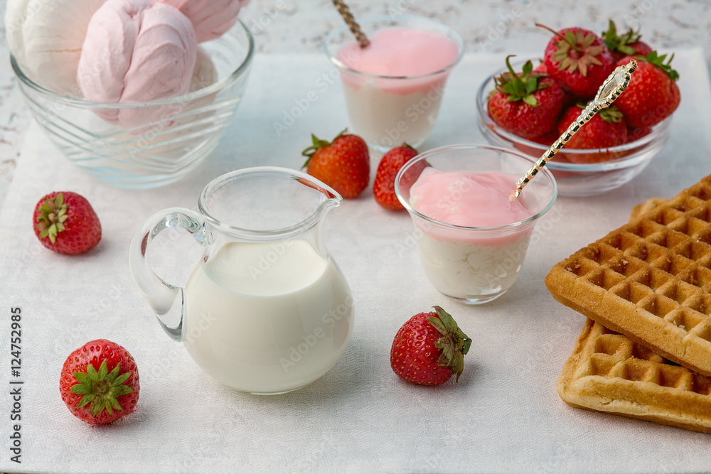 Food. On a white background, yoghurt, biscuits, milk, marshmallows, cookies, cheese, strawberry. In a glass container. Strawberries scattered on the table. Food. On a white background, yoghurt, biscuits, milk, marshmallows, cookies, cheese, strawberry. In a glass container. Strawberries scattered on the table.