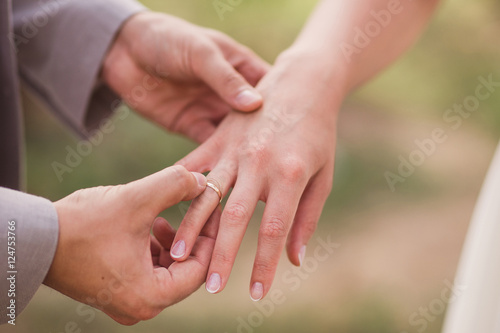 Closeup of a groom putting a gold wedding ring onto the bride's finger