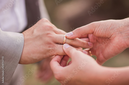 Closeup of a bride putting a gold wedding ring onto the groom's finger