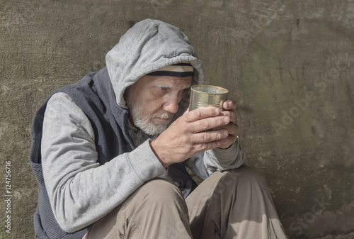 Portrait image of a mature homeless man sitting outdoors with a tin can photo