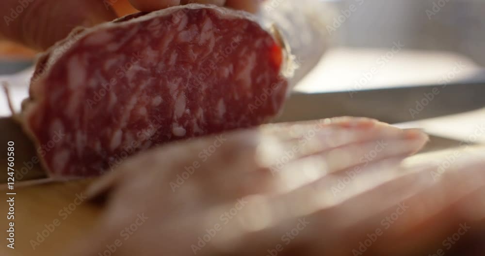 An experienced chef in a professional kitchen cuts the salami seasoned.Il Italian salami sausage is cut with a professional knife with very thin slices. the concept of nature, Italy, food, diet and bi