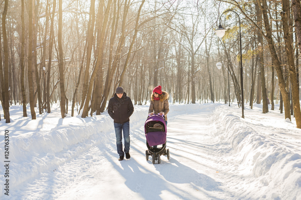 Happy young family walking in the park in winter. The parents carry the baby in a stroller through the snow.