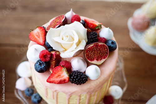 Cake with various berries, figs, meringues and rose on top.