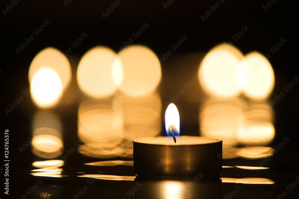 Single candle burning in darkness with reflection of candlelight in the background Single candle burning in darkness with reflection of candlelight in the background