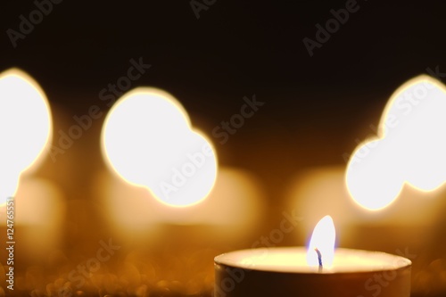 Burning candle against golden candlelight background