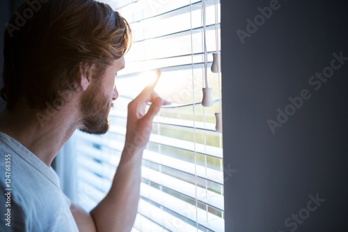 Man looking through window blinds after waking up © WavebreakMediaMicro