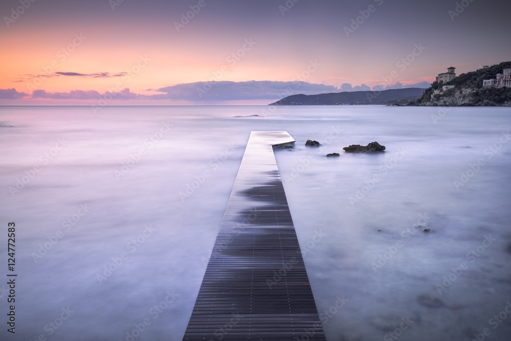 Castiglioncello bay wooden pier, rocks and sea on sunset. Italy
