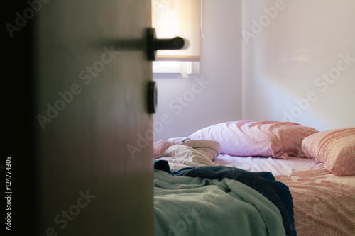 Fotografi Unmade bed with sunlight from the window and door ajar
