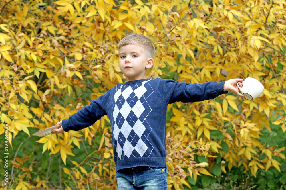 beautiful blond smiling small boy holds a cup in nature.
