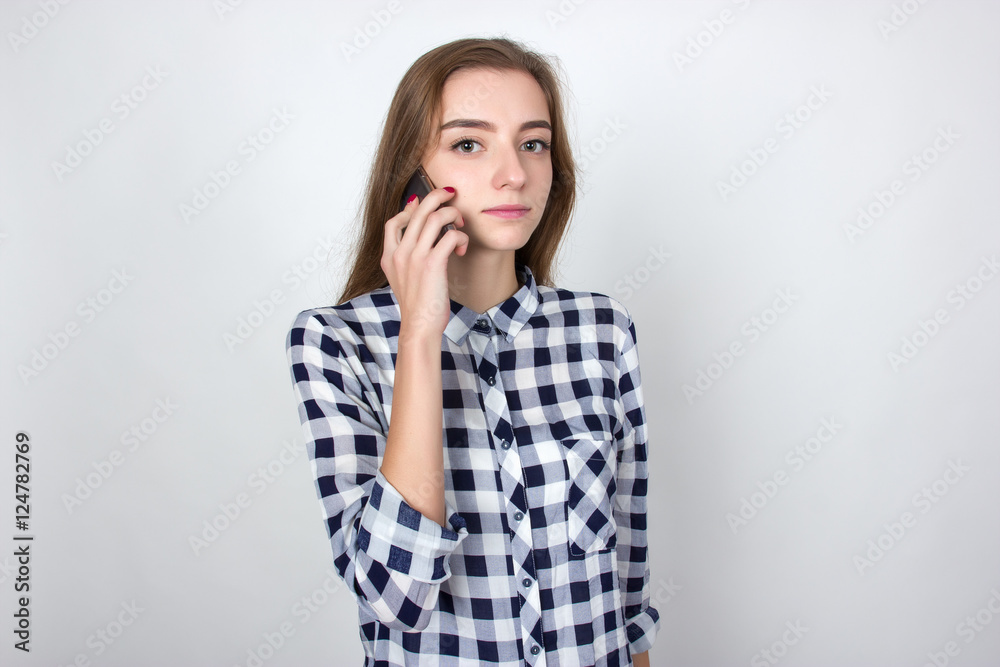 Portrait of a pretty woman in plaid shirt using a cell phone standing over gray background and looking at camera Portrait of a pretty woman in plaid shirt using a cell phone standing over gray background and looking at camera