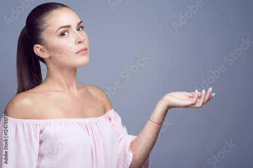 Φωτογραφία Portrait of beautiful dark-haired girl with perfect skin and nude make up showing empty palm proposing a product