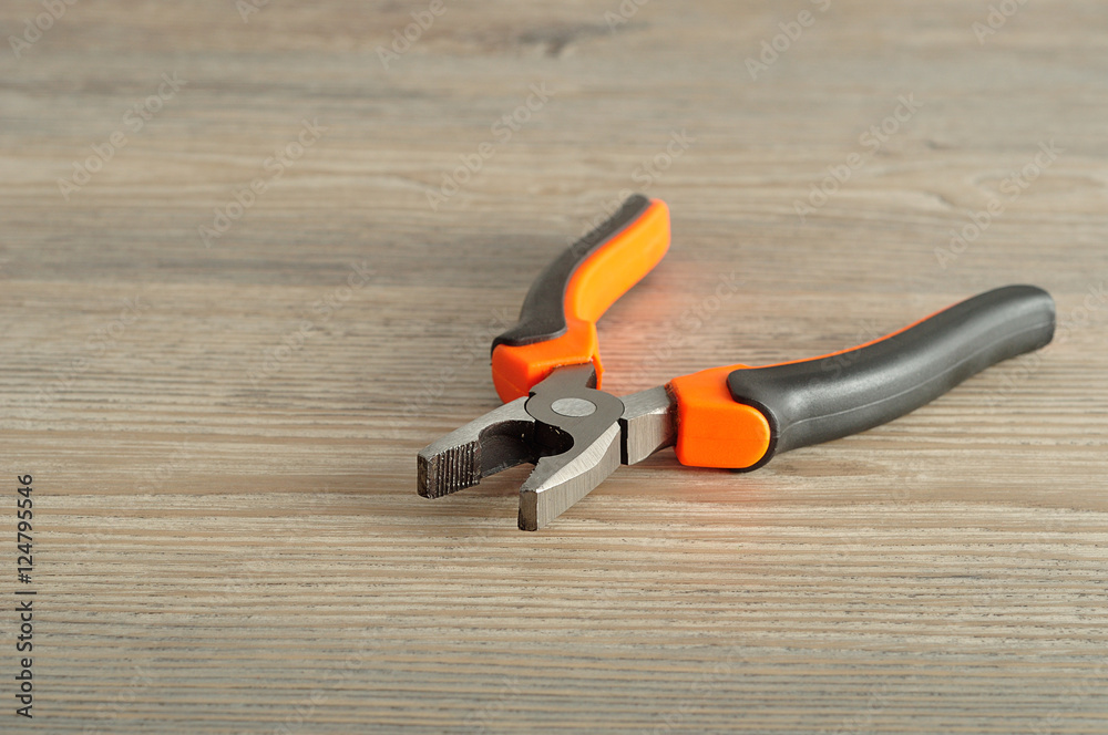 An orange and black pliers isolated on a wooden background