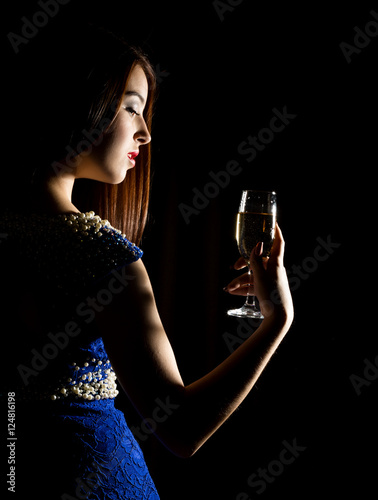 Young celebrating woman in a blue dress holding a glass of champagne on a dark background. play of light and shedow photo
