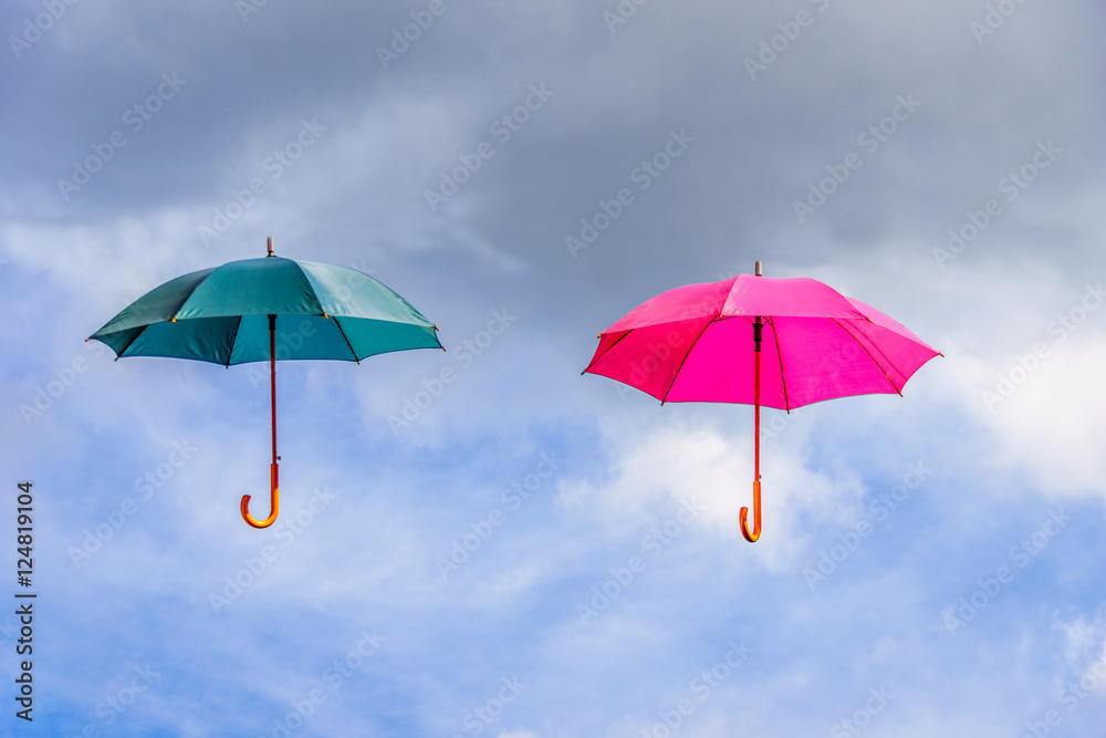 Pink and green umbrella or parasols floating suspended in the air under cloudy sky