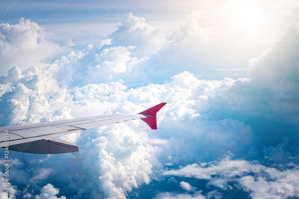 Fototapeta premium cloudy sky and red airplane wing as seen through window on aircr