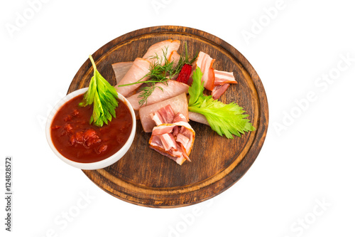 Meat cold cuts, cured sliced pork on wooden board with red chili sauce