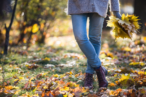 Female legs in jeans and boots, armful of leaves. Autumn scene