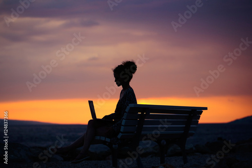 woman with laptop on evening beach