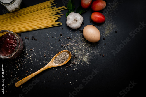 Food frame. Pasta ingredients - tomatoes  garlic  herbs  salt  spaghetti pasta and egg on black grunge background with copy space  Top view