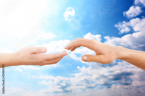 Female and male hands reaching to each other on sky background. Help and care concept.