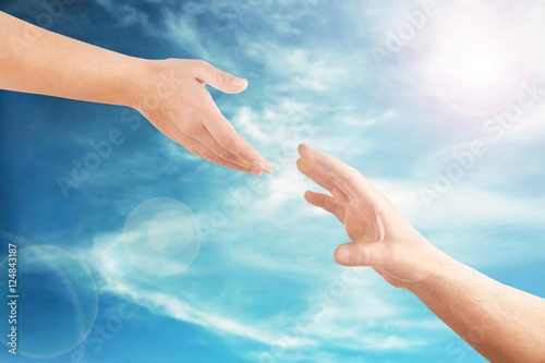 Female and male hands reaching to each other on sky background. Help and care concept.