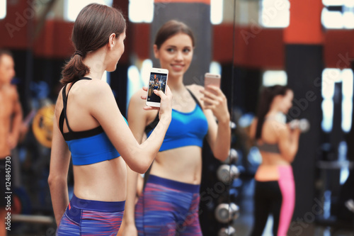 Young sportive woman taking selfie near mirror in gym