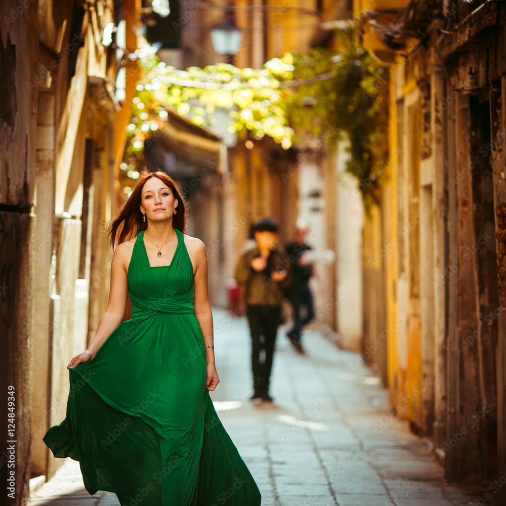 Red-haired lady spreads her dress while walking along an old str