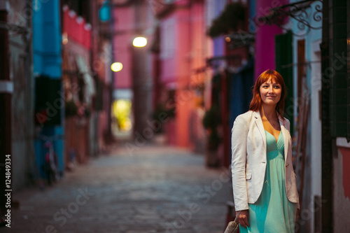 Lady in mint dress and white jacket walks along an old street