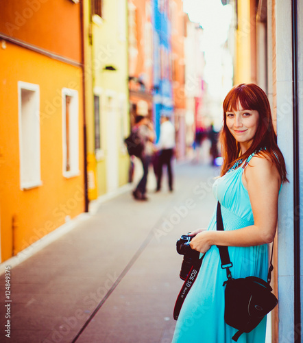 Smiling lady in blue dress holds a camera while standing on the © pyrozenko13