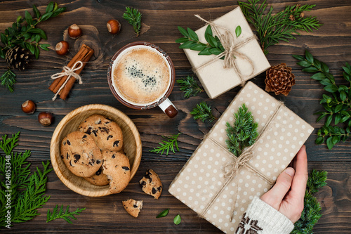 Opening Christmas present. Woman's hands holding decorated gift box on rustic wooden table. Ideal Christmas morning breakfast. Overhead, flat lay, top view