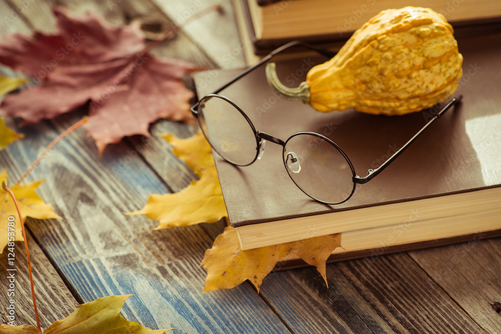 Eye glasses with book and autumn leaves on table