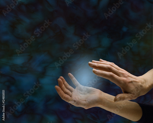 Paranormal activity - female hand sensing small blue orb between hands  on a dark black and blue energy formation background with copy space all around photo