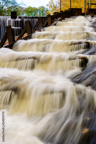 Fish ladder with rapids in fall. Water flowing in steps is helpful for migrating fish to overcome the dam visible in the background.