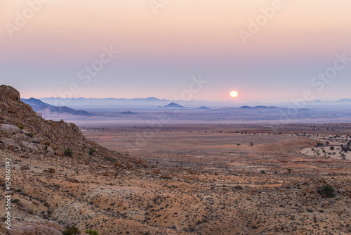 Colorful sunset over the Namib desert, Aus, Namibia, Africa. Orange red violet clear sky at the horizon, glowing rocks and canyon in the foreground.