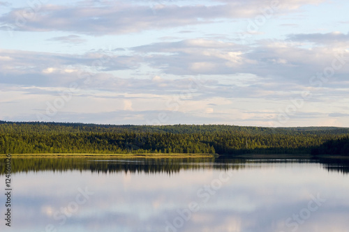 Russia. Karelia. Chupa. Bay of the White Sea. Landscape. Pine forest on the shore. Reflection in water. Cumulus clouds.