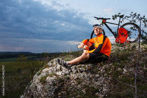 Cyclist resting on grass in mountains. Man is looking aside.