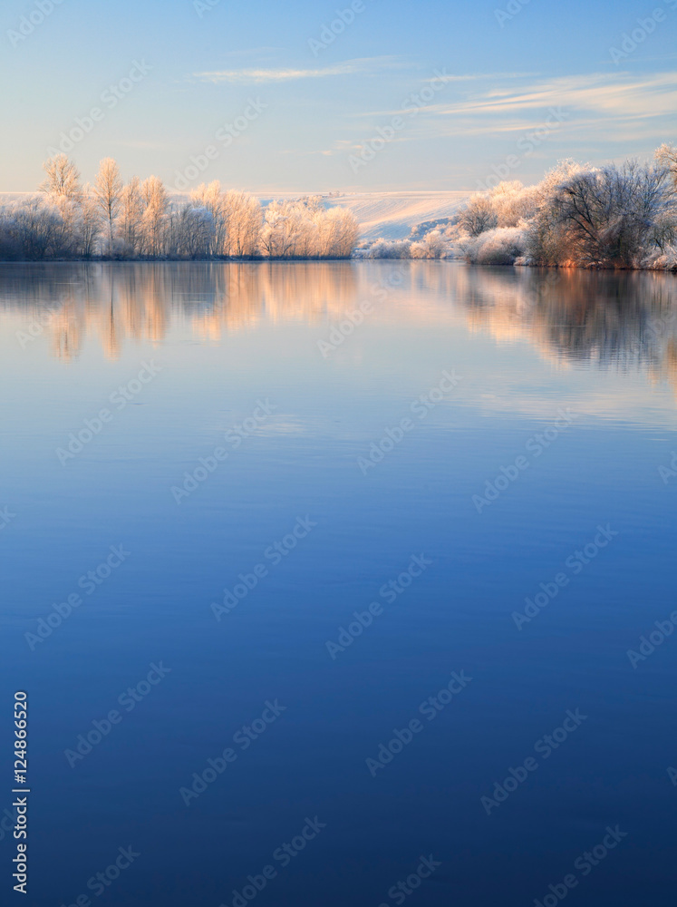 Winter Landscape Reflecting in River at Sunrise, Trees covered by hoarfrost and snow, blue sky, space for text Winter Landscape Reflecting in River at Sunrise, Trees covered by hoarfrost and snow, blue sky, space for text