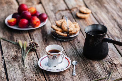 Cup of coffee and pot with different tasty snacks on wood. Ol rustic table served for traditional turkish coffee break with sweet cookies and fresh plums