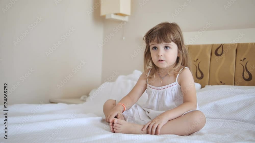 Adorable child in white dress watching tv on the bed Adorable child in white dress watching tv on the bed