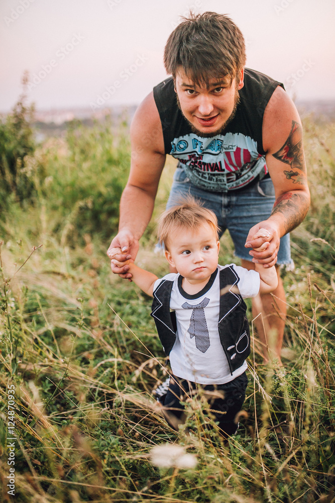 Fototapeta premium happy joyful father having fun throws up in the air his small child, family, father's day - concept. On the nature near the old retro car. Man has tatoo