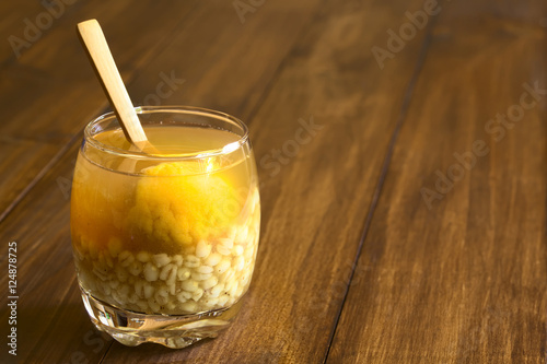 Traditional Chilean summer drink Mote con Huesillo, made of dried peaches, cooked husked wheat, cinnamon and sugar, photographed with natural light (Selective Focus, Focus on the front of the drink) photo