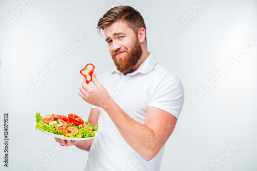 Man holding slice of red papper and plate with salad