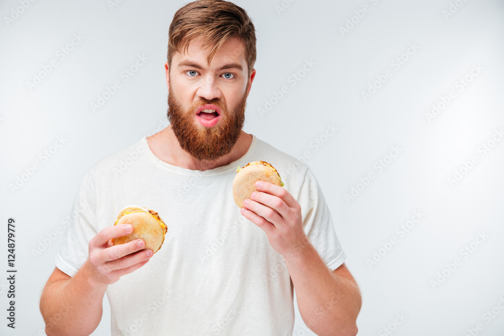 Hungry young bearded man holding two hamburgers Hungry young bearded man holding two hamburgers