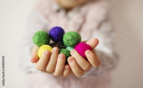 Close up of children hands holding colorful felt balls. Child, kid palms. A little girl keep in handfuls of colored wool balls. Lifestyle concept. Selective focus