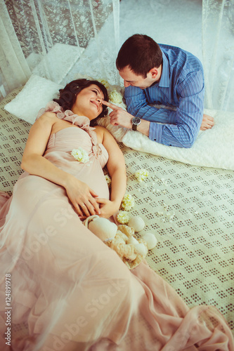 Man in blue shirt leans to a pregnant woman while she rests on w