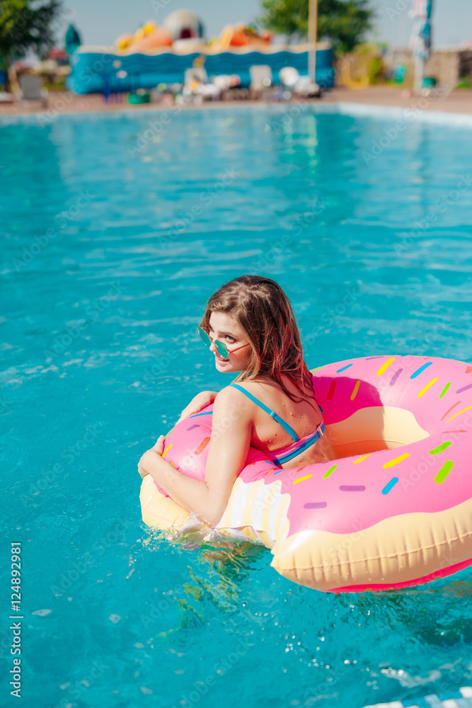 Young girl in sprinkled donut float at pool 20s