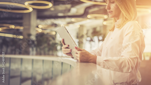 Side view, of a girl with blonde hair in a light pink shirt standing and holding a tablet computer.Business woman checks email on a tablet computer.Selective focus, film effect, blurred background. photo