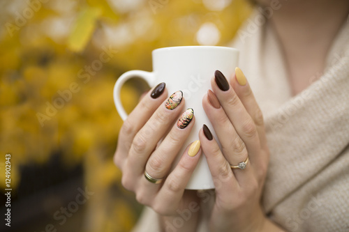 hands of autumn nails holding a cup of hot tea